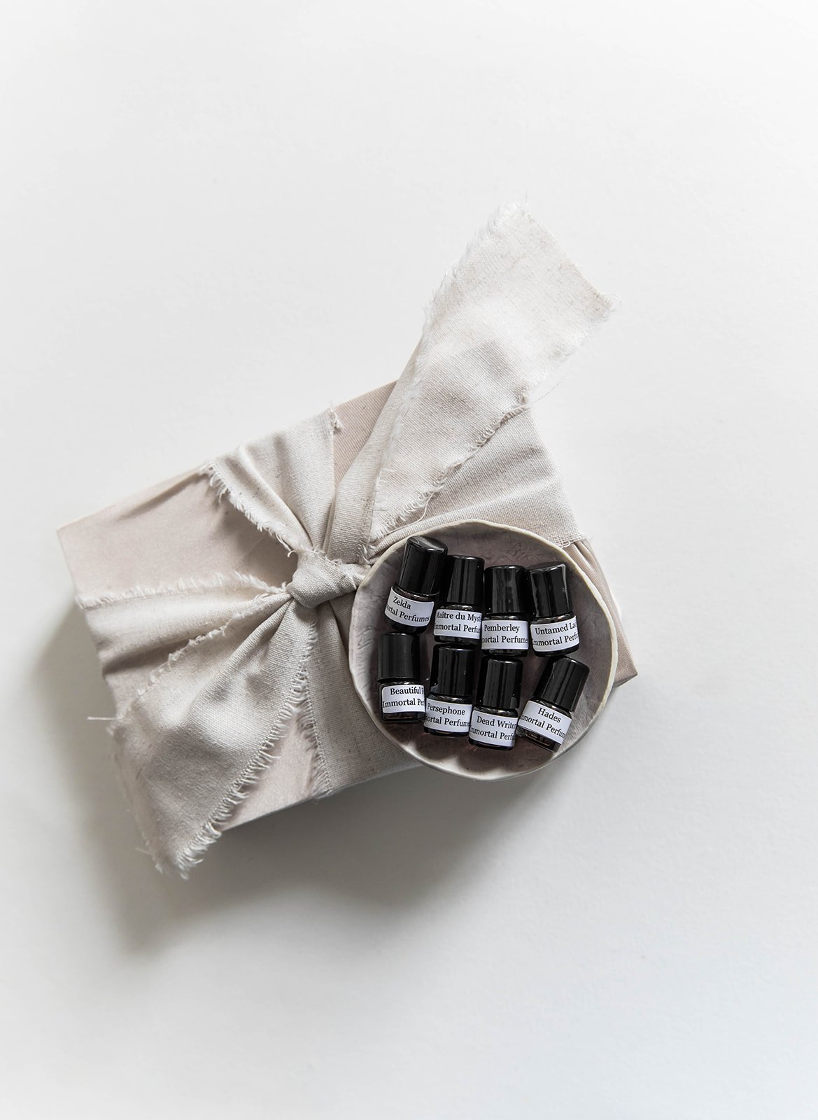 Small black Immortal Perfumes sample bottles in a dish beside a ribbon-wrapped gift.