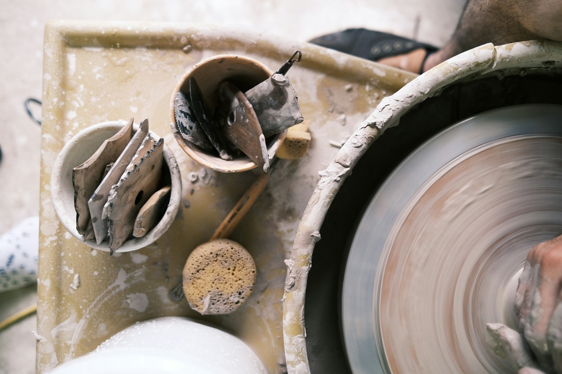 Pottery tools and a sponge beside a rotating wheel where a hand shapes clay.