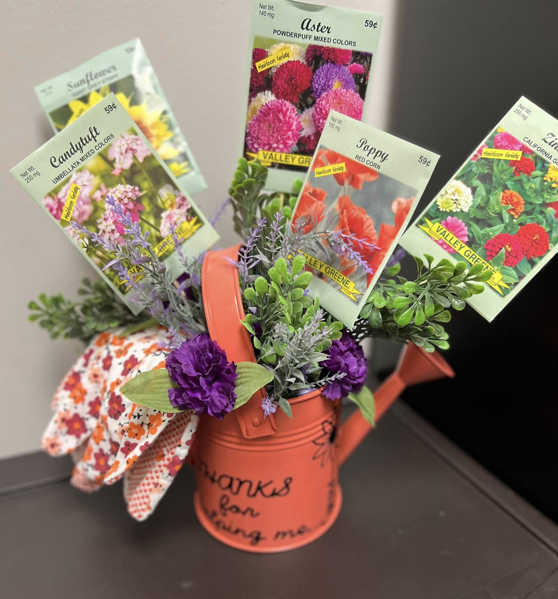 Seed packets, gardening gloves and flowers arranged in an orange watering can as a teacher-appreciation gift.